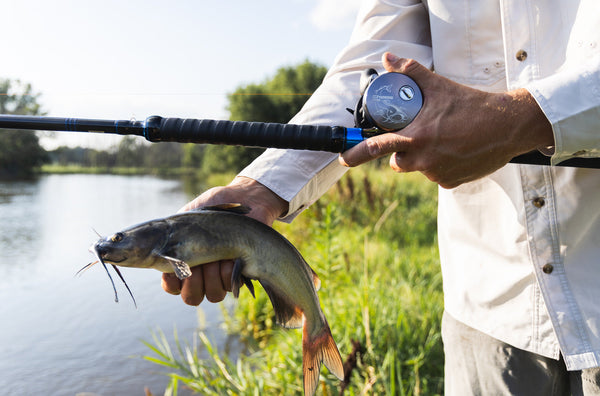 A man holding a fish and his fishing reels